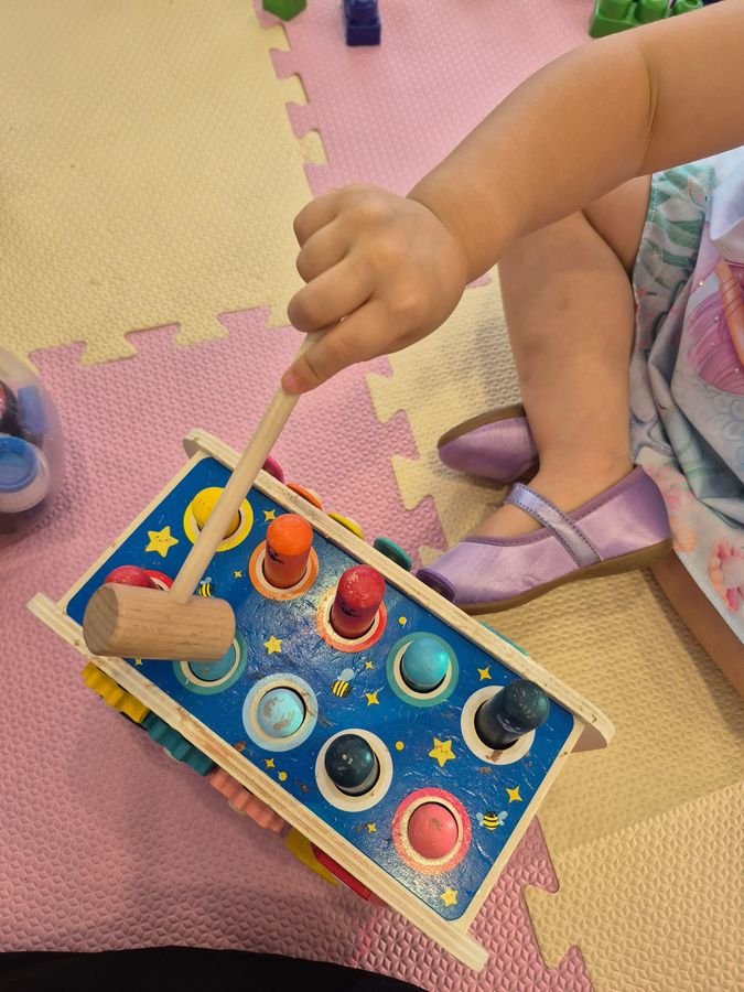 Bebê brincando com brinquedo sensorial de martelinho sobre tatame rosa