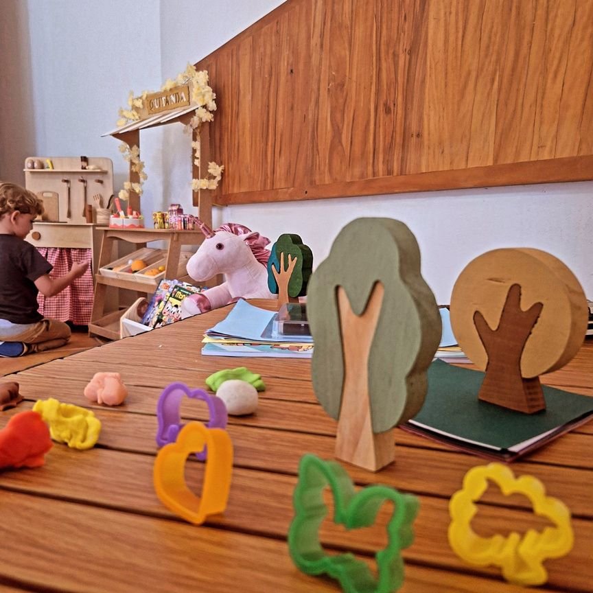 Mesa com brinquedos de madeira, árvores e massinha durante a recreação