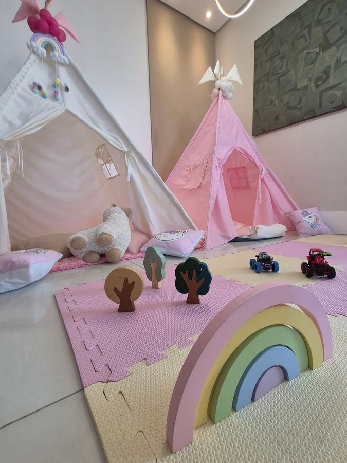 Teepee rosa com arco-íris de madeira e brinquedos sobre tatame